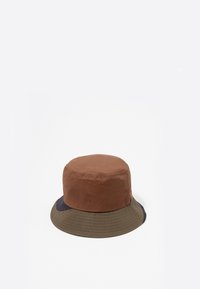 Gorra de cubo marrón y verde con la parte superior redondeada, tejido texturizado y un ala ancha. Presenta un diseño bicolor con costuras horizontales.