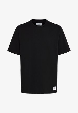 Melna īsām piedurknēm T-krekls, izgatavots no kokvilnas, ar apļa kakla izgriezumu un nelielu baltu etiķeti ar drukātu tekstu kreisajā apakšējā stūrī.