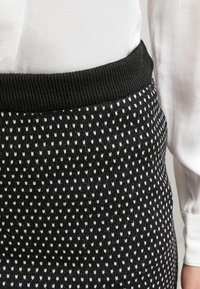 Jupe en tricot avec une base noire et un motif blanc de petites formes. Présente une taille en côtes noires, mettant en valeur la texture et le détail du design.