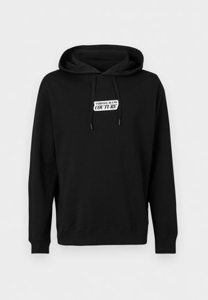 Μαύρο φούτερ με κουκούλα, μπροστινά κορδόνια και λευκή ορθογώνια ετικέτα με το λογότυπο "Versace Jeans Couture".