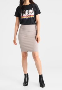 Camiseta gráfica negra con el texto "loved" y rayas multicolores, combinada con una falda ajustada beige con un patrón de espiga y botines negros.