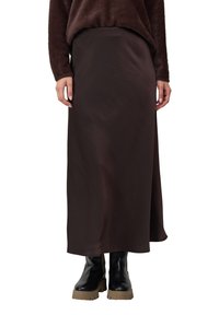 Femme portant une jupe midi marron foncé, un pull en laine épaisse marron foncé et des bottes chevilles à semelle épaisse noires, se tenant devant un fond blanc.