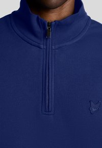 Pullover blu navy con mezza cerniera realizzato in tessuto strutturato. Presenta un piccolo logo ricamato sul petto a sinistra e una cerniera robusta.