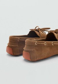 Scarpe in camoscio marrone con punta arrotondata, dettagli con lacci e tacco in gomma tan a contrasto. Presentano occhielli in metallo e sottili accenti di cucitura.