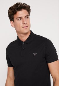 Sort polo skjorte lavet af bomuld, med en krave-design, to-knap lukning og et lille broderet logo på brystet.