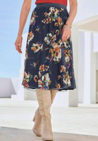 Florale A-lijn rok met een marineblauwe achtergrond, versierd met heldere oranje, gele en groene bloemen, gecombineerd met beige kniehoge laarzen.