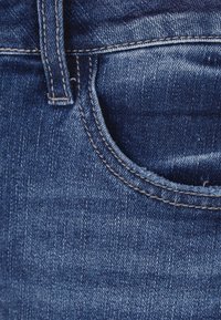 Primer plano de un bolsillo de jeans de mezclilla, con un color azul intenso, costuras visibles y un ligero desgaste en la textura de la tela alrededor de la abertura.