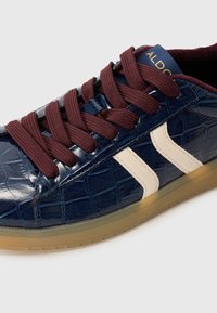 Navy blå faux krokodillelær sneaker med creme striber, burgunder snørebånd og en gennemsigtig gummisål. ALDO-logo på tungen.