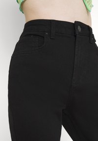 Zwarte denim high-waisted broek met voorzakken, riemlussen en een knoopsluiting. Gladde textuur met een stevige afwerking.