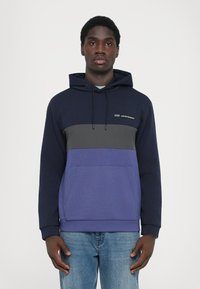 Sweatshirt azul marinho e cinza em tecido misto, com bolso canguru frontal, capuz com cordão e design de blocos de cor horizontal.