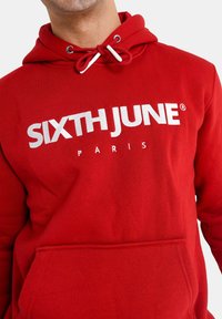 Sudadera roja de algodón, con un bolsillo tipo canguro, capucha ajustable con acentos blancos y el nombre de la marca impreso en blanco, "SIXTH JUNE PARIS."