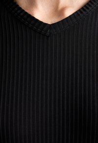Haut en tissu côtelé noir avec un décolleté en V, présentant des rayures verticales et une finition texturée, mettant en valeur une silhouette ajustée.