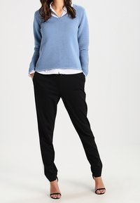 Lys blå ribbestrikket sweater med V-hals, lagd over en hvid skjorte med krave; parret med sorte skræddersyede bukser og sorte højhælede sko.