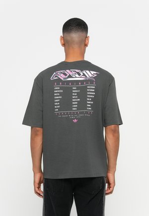 Man with short hair facing away wearing a dark gray t-shirt with pink and white European city names and graphic text.