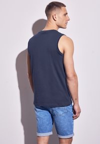 Mörkblå ärmlös skjorta i bomull, tillsammans med ljusblå denimshorts med uppvikta fållar och bakfickor.