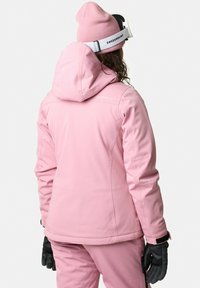 Giacca da sci rosa con cappuccio, realizzata in tessuto liscio. Dotata di tasche laterali, polsini regolabili e un fit rilassato. Abbinata a un berretto rosa.