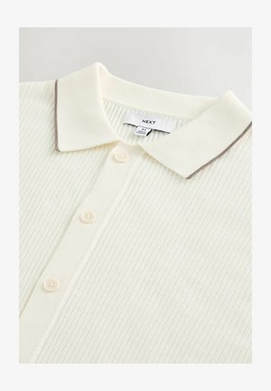 Tejjel színezett póló, textúrált bordázott mintával, kontrasztos barna díszítéssel a galléron és öt gombbal az elején.