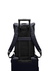 Sac à dos bleu marine avec des bretelles rembourrées, une poignée réglable et un tissu texturé. Attaché à une valise à roulettes bleu foncé, montrant un design élégant.