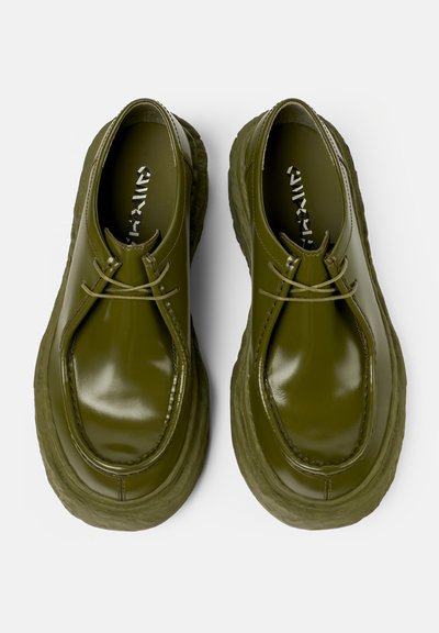 Green leather shoes with a glossy finish, featuring a rounded shape, textured sole, and matching laces. Minimalist design with no embellishments.