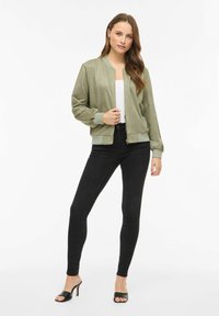 Bojówka oliwkowo-zielona z zamkiem błyskawicznym z przodu, ściągaczami na mankietach i u dołu. Nosi się ją na biały top, w połączeniu z czarnymi dopasowanymi jeansami i czarnymi mule na obcasie.