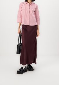 Randig röd och vit skjorta med trekvartsärmar, kombinerad med en lång burgundyröd satinkjol och kraftiga svarta loafers.