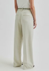 Pantaloni larghi beige chiaro con una vestibilità rilassata, dotati di una cintura nera e due tasche posteriori. Il materiale sembra essere testurizzato e traspirante.