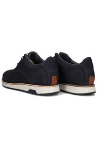 Marineblauwe schoenen van textuurmateriaal met een witte zool. Bevat bruine lederen accenten bij de hiel en het vetersysteem. Glad, afgerond ontwerp.