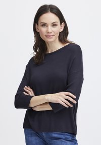 Jūras zila svīteris ar brīvu piegriezumu, apaļu kakla izgriezumu un trīs ceturtdaļu piedurknēm. Izgatavots no mīksta materiāla ar ribotu tekstūru malās.