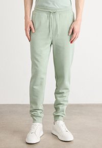 Pantalones de chándal de color verde claro, hechos de una suave mezcla de algodón, con una cinturilla elástica y cordón, además de bolsillos laterales.