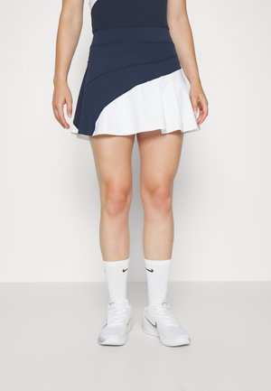 Falda atlética en azul marino y blanco con un diseño curvado, que presenta una textura suave, dobladillo acampanado y cintura elástica. Combinada con calcetines y zapatos blancos.