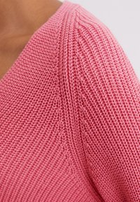 Roze gebreide trui met een gestructureerd ontwerp met verticale ribbels en een v-halslijn, gemaakt van een zachte, lichte stof.