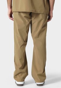 Pantalones beige, ligeros y de corte relajado, con una textura suave y un diseño sencillo. El dobladillo queda por encima de unas zapatillas blancas.
