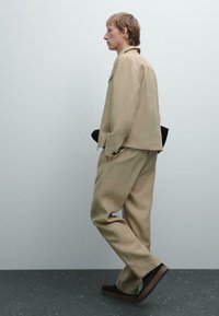 Giacca beige su misura e pantaloni coordinati realizzati in tessuto morbido, con una vestibilità rilassata. Calzature nere con una suola spessa. Design semplice e minimalista.