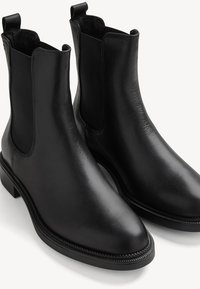 Bottines en cuir noir avec panneaux latéraux élastiques et languettes de tirage, avec un talon bas empilé et un design à bout arrondi.