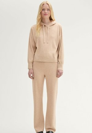 Sudadera beige con cordón, corte relajado y mangas largas, combinada con pantalones de pierna ancha a juego, fabricados en una suave tela texturizada.