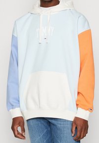 Felpa con cappuccio caratterizzata da blocchi di colore blu chiaro, arancione e bianco, tasca frontale e logo "TOMMY". Tessuto morbido e polsini a costine.