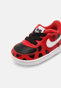 Červené kožené tenisky s černými akcenty a puntíky. Obsahují bílé logo Nike a černé tkaničky. Malý, zaoblený design s texturovanými povrchy.