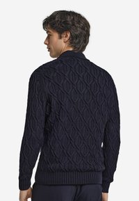 Mörkblå stickad tröja med ett strukturerat diamantmönster, ribbade ärmslut och nederkant. Designad med en hög krage och en åtsittande silhuett.