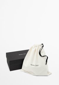 Sac en coton avec cordon de serrage en blanc cassé et accents noirs, à côté d'une boîte noire avec du texte blanc. Formes simples et rectangulaires.