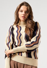 Suéter de punto con cuello vuelto acanalado, patrones ondulados en beige, marrón, azul marino y negro; mangas globo con detalle de leve gather.