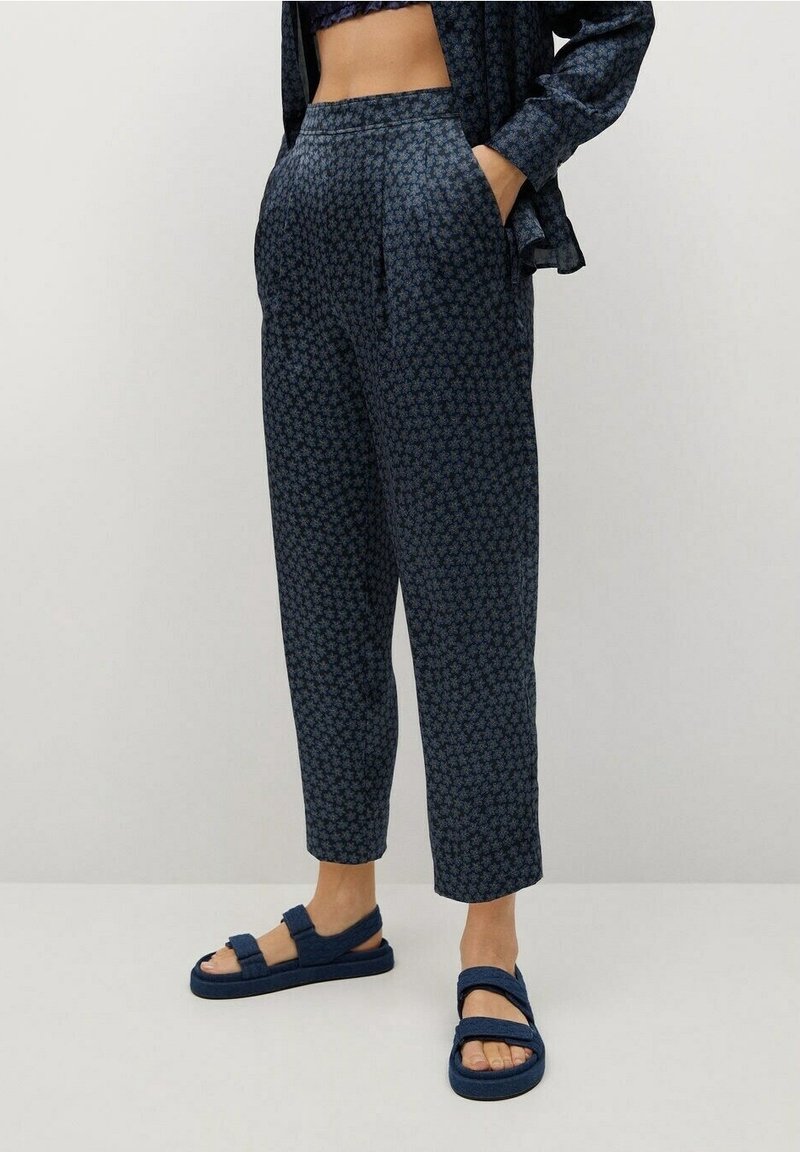 Person, die hoch taillierte, verkürzte marineblaue Hosen mit kleinem Blumenmuster trägt, dazu ein passendes langärmliges Hemd und marineblaue Sandalen mit offenen Zehen und Riemen.