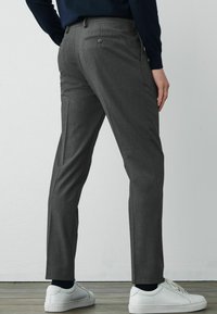 Pantalones de mezcla de lana grises con un ajuste entallado, que cuentan con bolsillos laterales y traseros, combinados con zapatillas blancas.