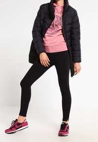 Chaqueta de pluma negra, sudadera rosa con diseño gráfico, leggings negros y zapatillas rosa/negra. Presenta una forma ajustada y una textura suave.