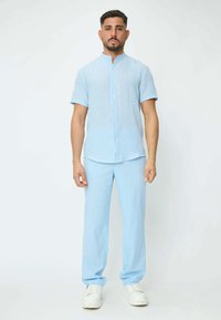 Chemise courte à manches bleues claires avec un motif rayé et un col mandarin, associée à un pantalon bleu clair assorti et des baskets blanches.