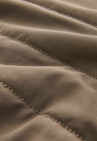 Rudas audinys su lygiu tekstūra, turintis įstrižus siūlus ir subtilius siuvinėjimo akcentus, kurianti užkloto išvaizdą.