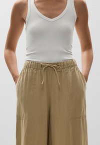 White ribbed tank top with a V-neckline paired with light beige drawstring wide-leg pants featuring side pockets and a textured finish.
