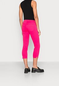 Jeans cortos rosas con bolsillos traseros, con un dobladillo ligeramente deshilachado. Combinados con mocasines negros que muestran una textura mate.