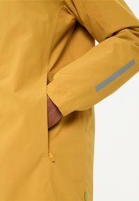 Giacca impermeabile gialla con una texture liscia, dotata di una tasca con zip sul lato e di una striscia riflettente sulla manica.