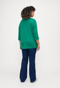 Grønn, oversized genser med trekvart ermer, kombinert med mørkeblå flagrende jeans. Genseren er laget av mykt stoff med jevn tekstur.