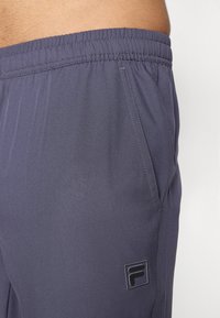 Marineblauwe sportshorts met een elastische tailleband, voorzien van een zijzak en een klein logopatch. Glad, lichtgewicht stof met een subtiele glans.